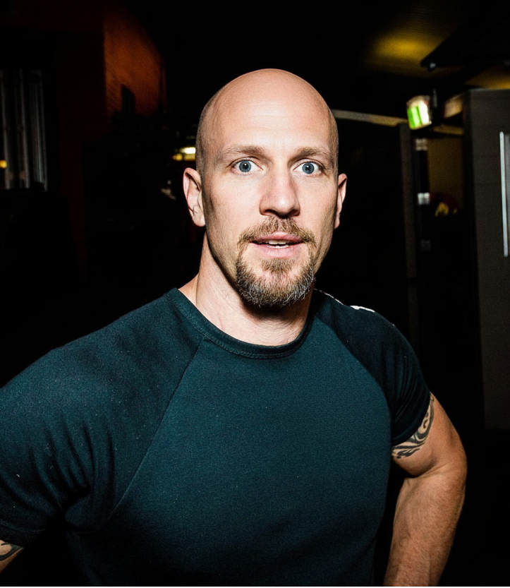 Man with tattoos wearing a dark shirt in a dimly lit room