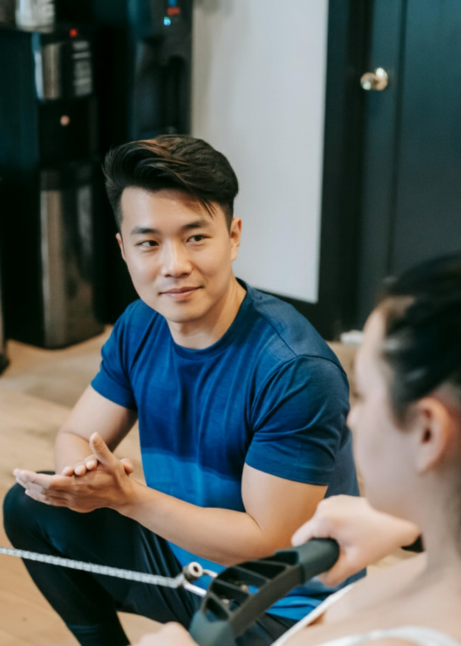 Man in blue shirt sitting with a woman in a white tank top in a gym setting.