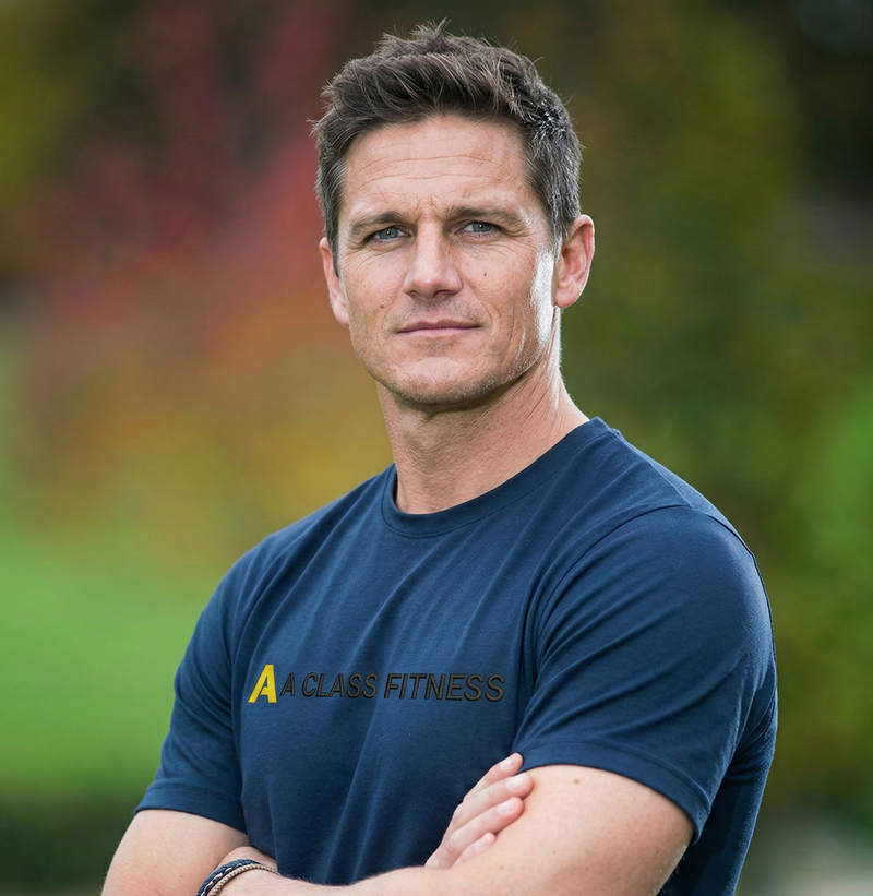 Man wearing a blue 'A Class Fitness' t-shirt with arms crossed outdoors.