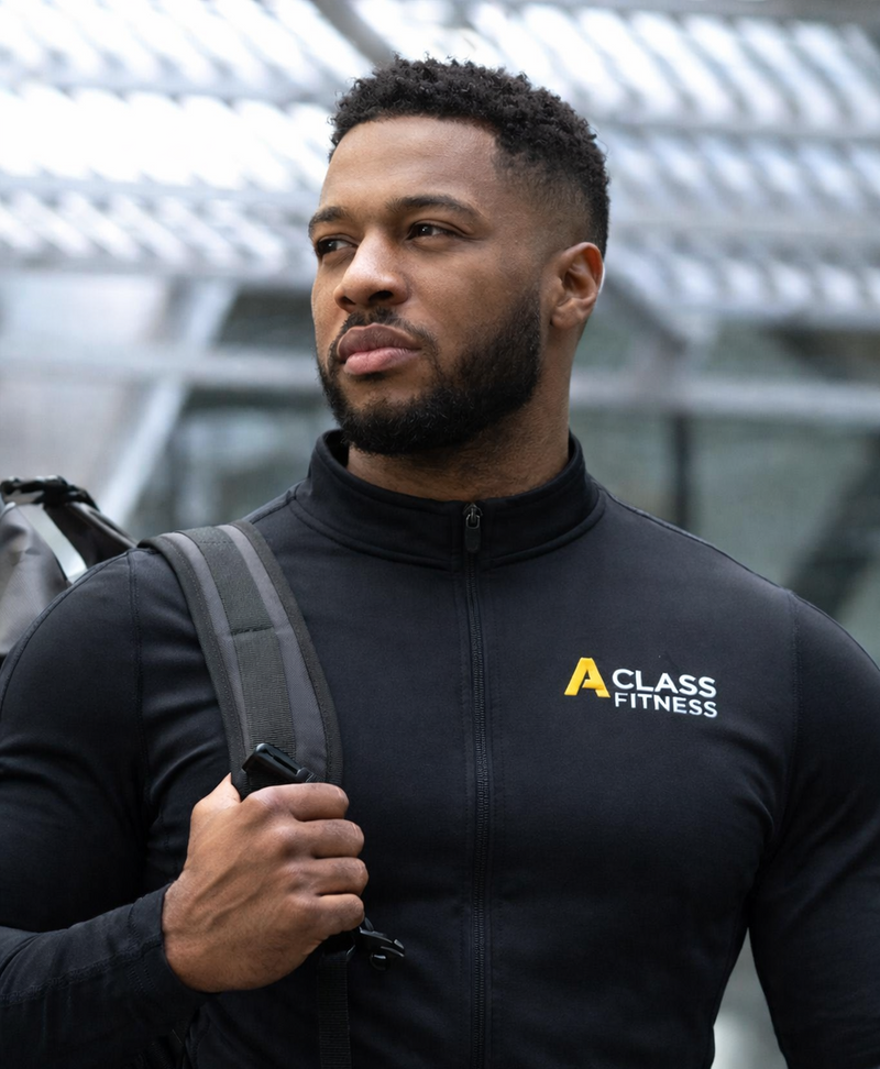 Man wearing a black jacket with Class Fitness logo, holding a backpack.