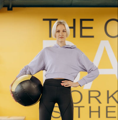 Woman holding a medicine ball in front of a yellow wall with text
