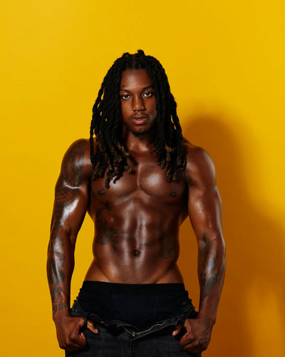 Muscular man with dreadlocks and tattoos on a yellow background
